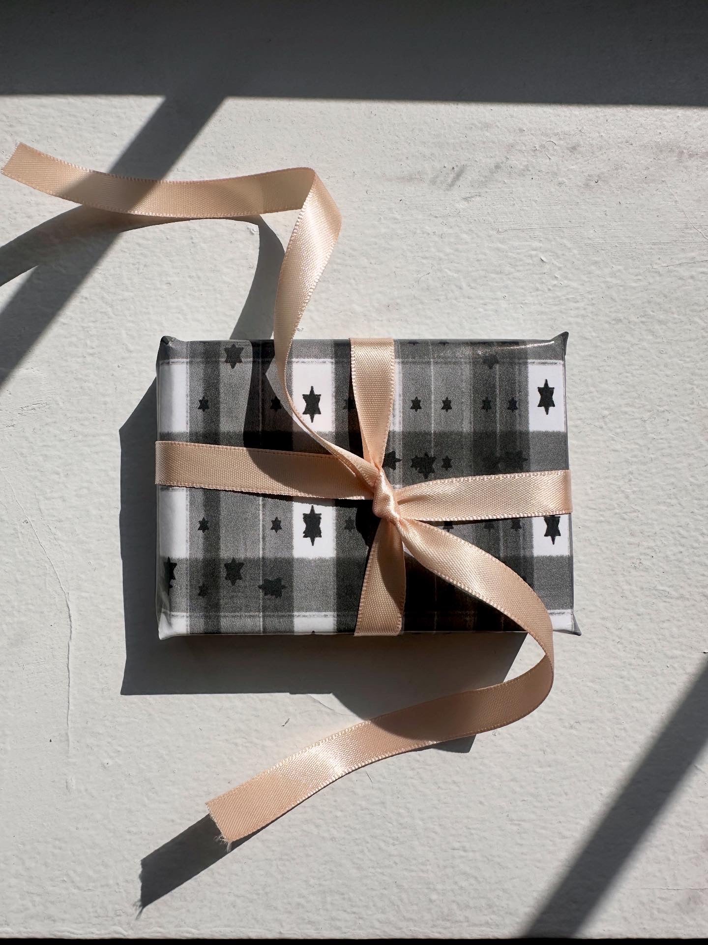 Jewish gift wrapping paper in black and white checkered paper with a pink ribbon on a light gray surface.